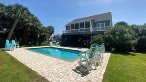 Una casa a due piani con piscina, circondata da palme e un prato curato.