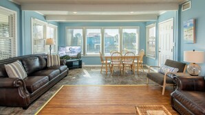 A living room with a brown leather sofa, a dining table with chairs, and a television.
