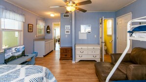 A room with a bed, a desk, a ceiling fan, a dresser, and a bunk bed.