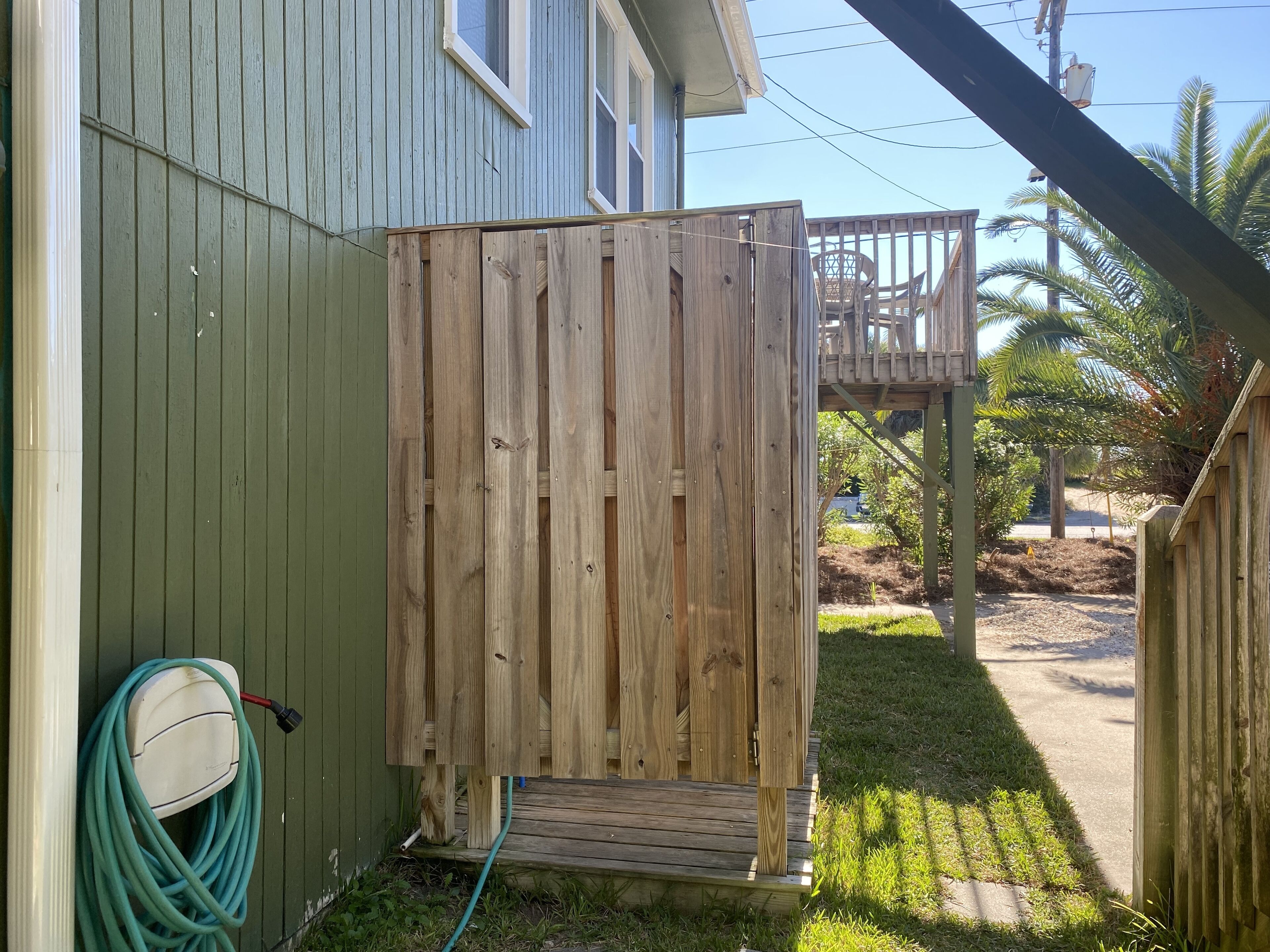 A wooden deck with a wooden gate, a hose, and a chair in the background.