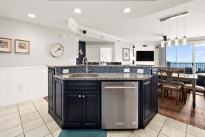 A kitchen with a central island, dark cabinetry, a stainless steel dishwasher, and a dining area with a view.