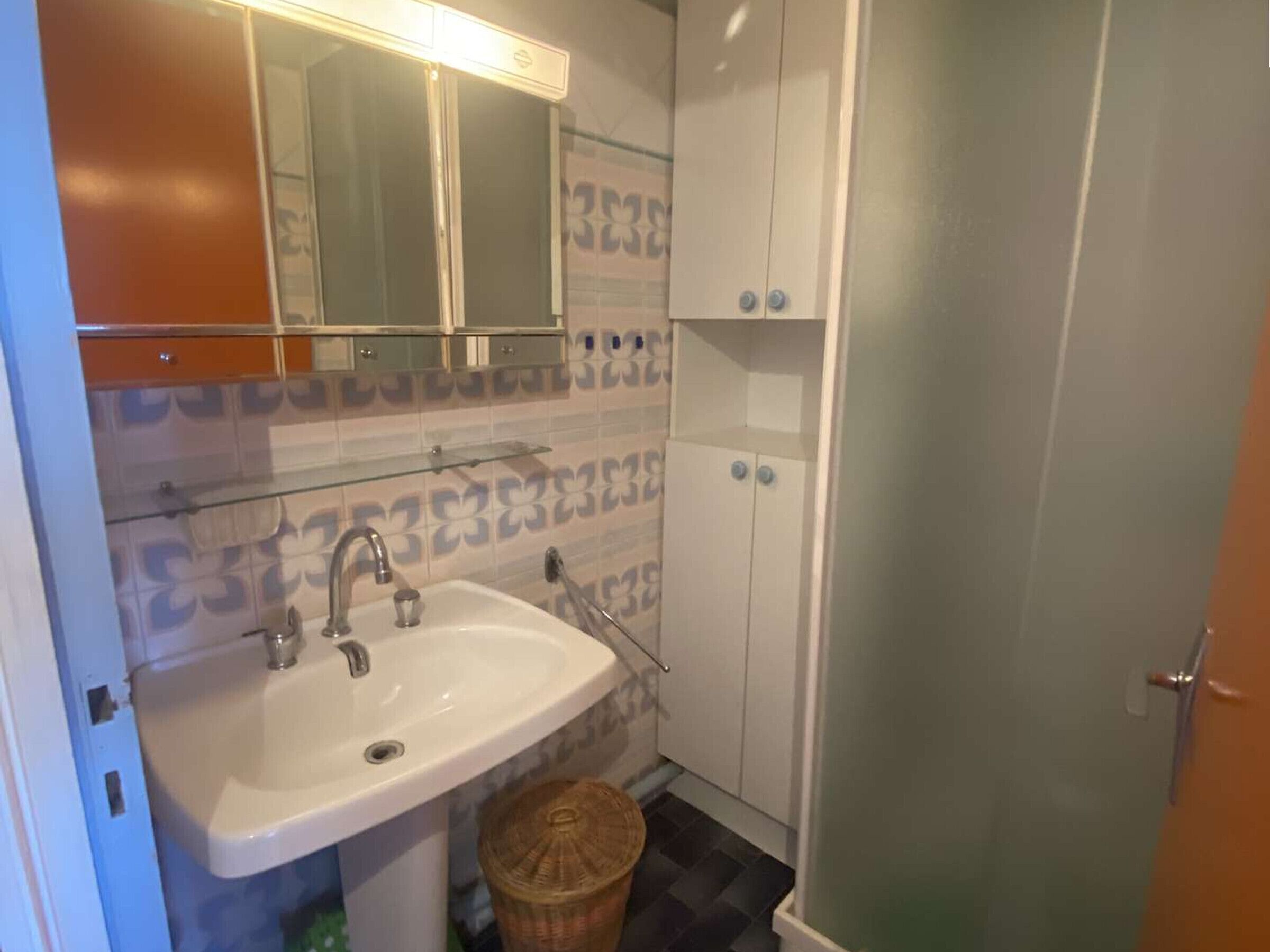 A bathroom with a white sink, a mirror above it, and patterned tiles on the walls.