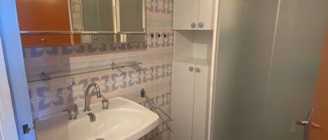 A bathroom with a white sink, a mirror above it, and patterned tiles on the walls.