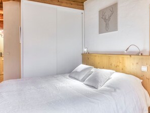 A bedroom with a wooden headboard, a bed with white bedding, a wall-mounted sink, and a framed deer head artwork.