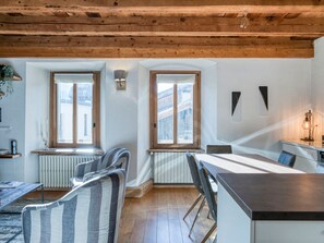 Un interior moderno con vigas de madera, una zona de comedor con mesa y sillas, y ventanas amplias.