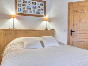 Quarto com cabeceira de madeira, duas luminárias de apoio, cama com roupa de cama branca e colagem de fotos na parede.