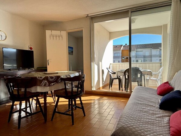 Ein Balkon mit Blick auf Gebäude, eine Essecke mit Tisch und Stühlen sowie eine Sitzecke mit Kissen.