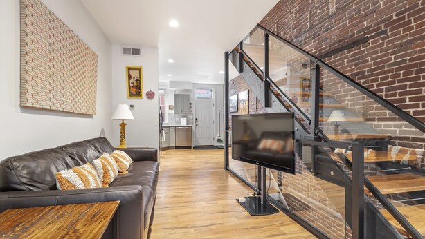 Een moderne woonkamer met een leren bank, een houten salontafel, een flatscreen televisie en een trap met glazen balustrades.