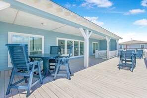 A covered outdoor deck with a table and chairs, a white railing, and a view of the ocean. - Ohana 3 Bedroom Home by RedAwning (Port Bolivar)