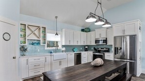 A modern kitchen with white cabinets, a dark wooden table, and stainless steel appliances.