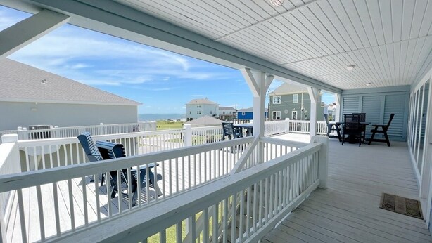 A covered outdoor deck with white railings and a table with chairs.