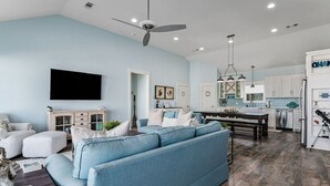 A spacious living room with a large blue sofa, a flat-screen TV, and a dining area with a wooden table.