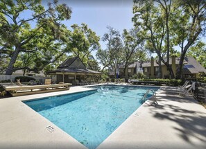 Relax by the serene pool surrounded by lush greenery and trees, with lounge chairs and a gazebo nearby.