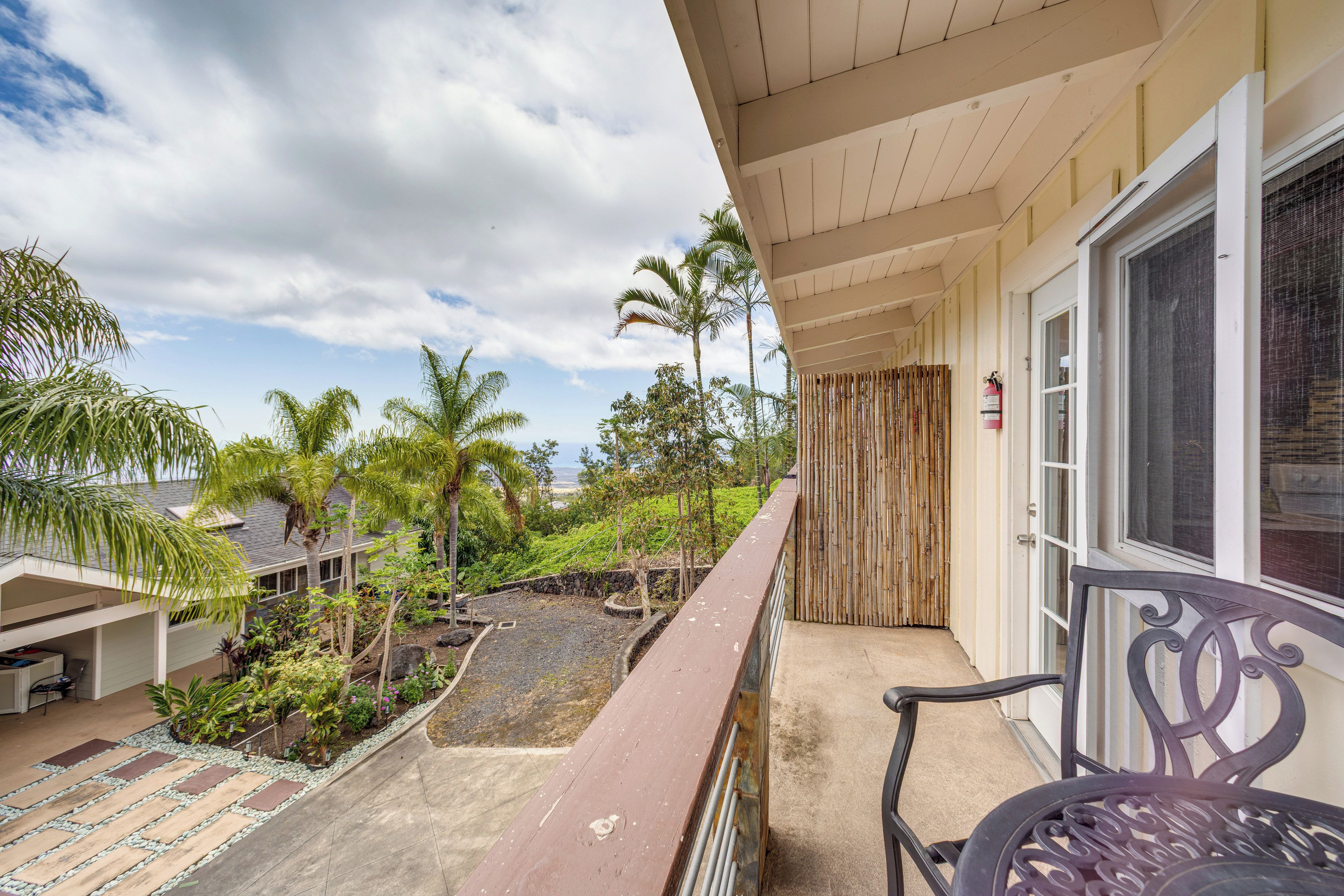 Un balcón con vista a un jardín ajardinado, un extintor y una silla.
