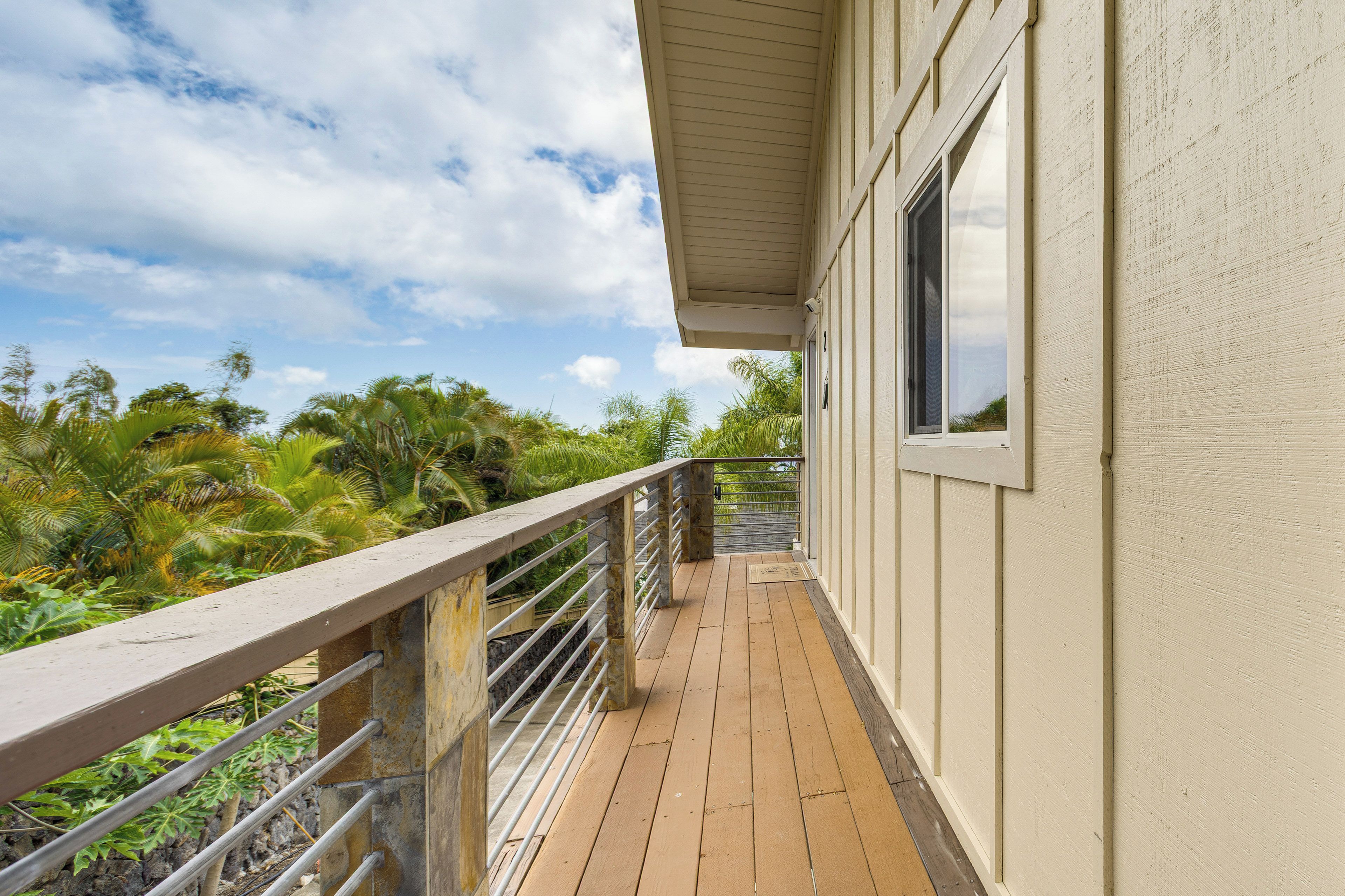 Una terraza de madera con barandillas de metal que conduce a un edificio de fachada color crema.