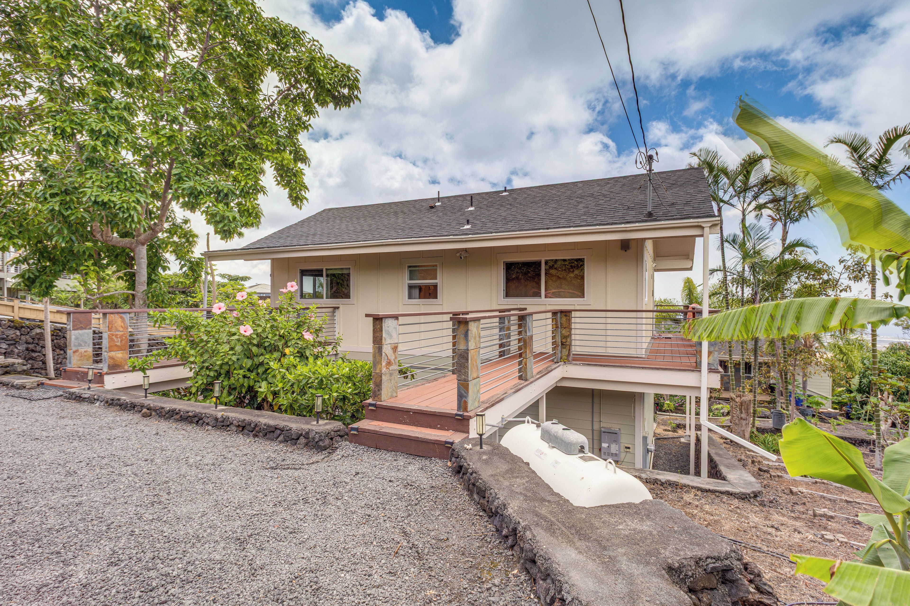 Une maison à deux étages dotée d’un balcon, entourée d’une végétation tropicale.