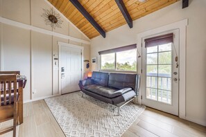 Una habitación con techo de madera, un sofá de cuero negro, una silla de madera, un tapete estampado y una puerta con ventanal.