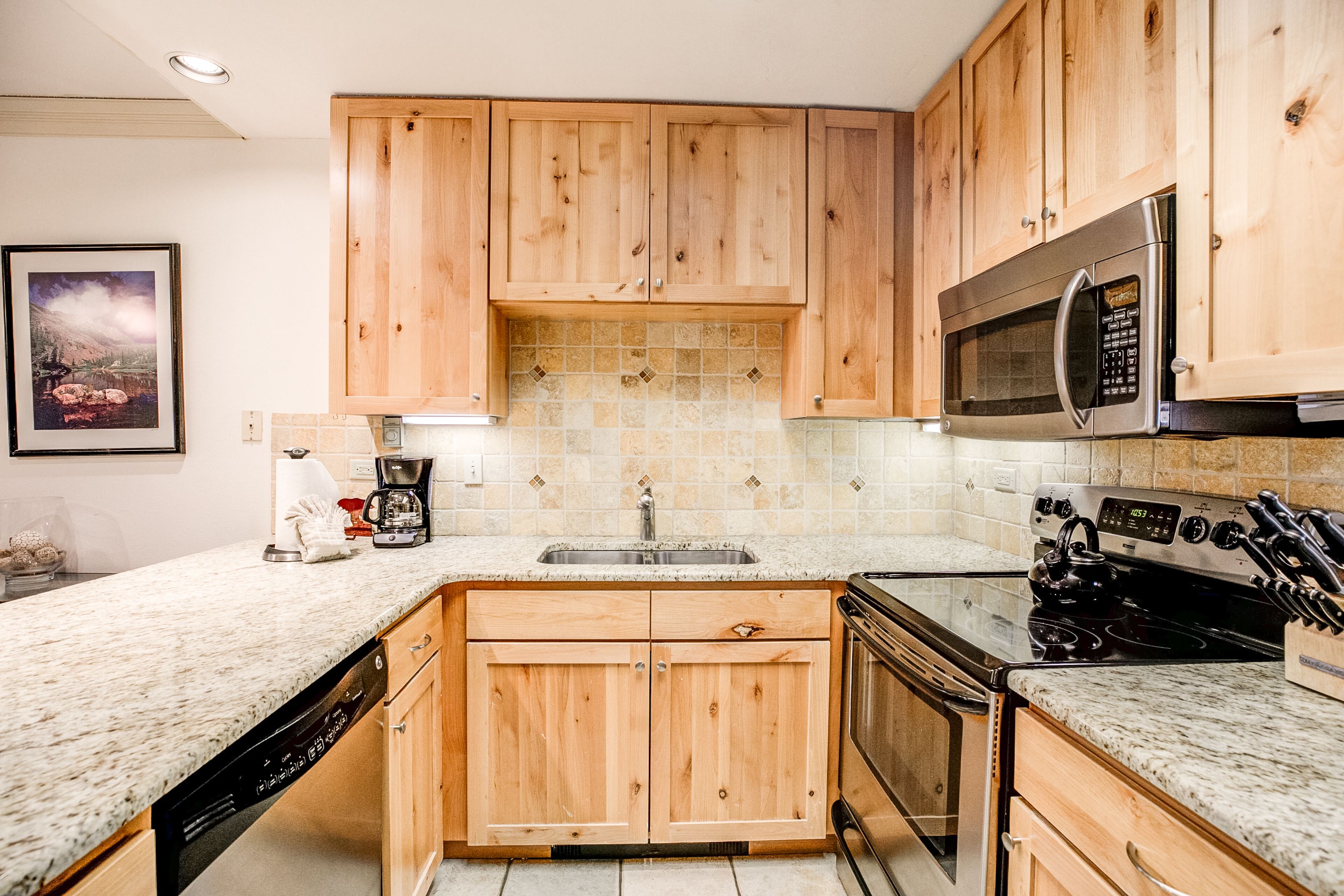 A kitchen with wooden cabinets, a stainless steel sink, a microwave, and a stove.