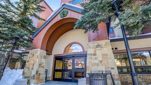 The Chateauaux hotel entrance with stone pillars, a snow-covered ground, and a Christmas wreath on the archway. - Village Chateaux Falcon SuperChair Condo: Great Location (Breckenridge)