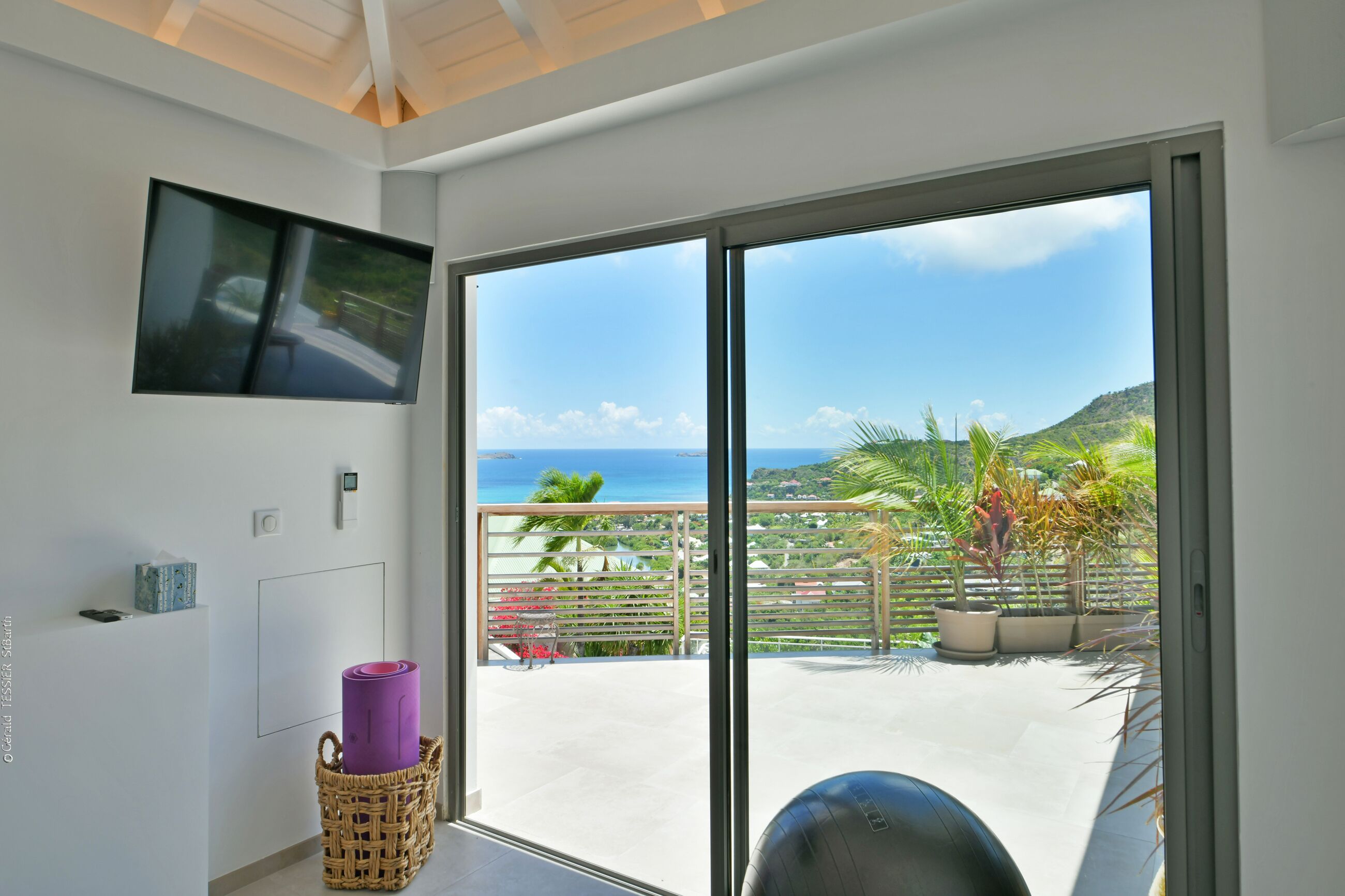 A balcony with a view of the sea, a mounted television, and exercise equipment.