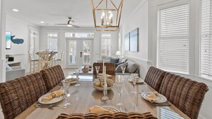 A dining area with a wooden table set for six, surrounded by wicker sofas, and a hanging light fixture above.