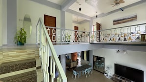 A spacious living area with a high ceiling, a staircase, a dining area, and a fireplace.