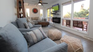 A living room with a grey sofa, ottoman, and a television on a stand.
