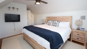 A bedroom with a bed, a ceiling fan, a TV mounted on the wall, and a bedside table with a lamp.