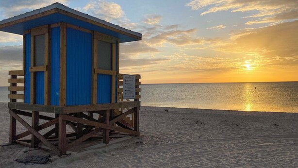Una postazione di salvataggio sulla spiaggia, con un cartello, affacciata su una spiaggia sabbiosa e l'oceano sullo sfondo.