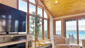 Een woonkamer met een televisie, een open haard, een plant en uitzicht op zee.