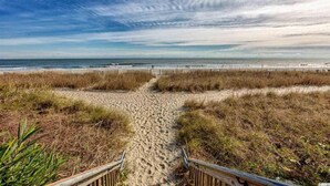 Un sentier de sable qui longe la plage et mène à l’océan, avec une clôture en bois d’un côté.