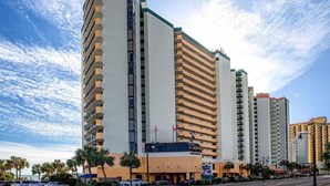 Un hôtel à plusieurs étages, doté d’un design moderne, avec une entrée imposante, une marquise bleue et un drapeau.