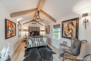 A bedroom with a large bed, a chair, a rug, and artwork on the walls. - Glamping in Spicewood TX Hill Country~ Cabin 1 The Madison at Green Acres (Spicewood)
