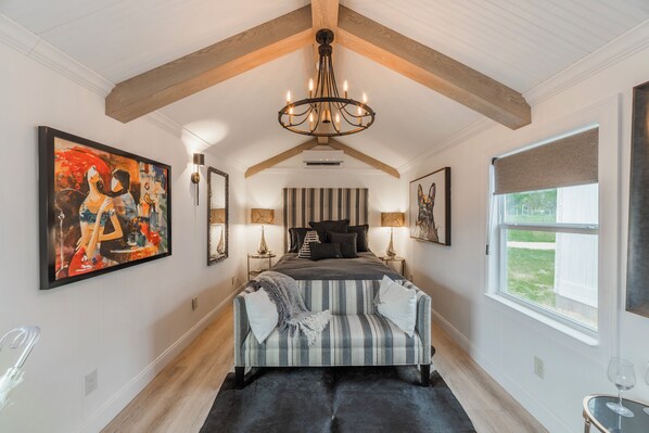 A bedroom with a bed, a chandelier, a window, and artwork on the walls. - Glamping in Spicewood TX Hill Country~ Cabin 1 The Madison at Green Acres (Spicewood)