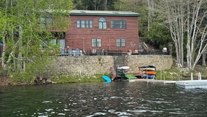 A wooden house with a stone wall, a dock with kayaks, and a calm body of water. - Heart Lodge,slg fam sleeps 11, Lakefront great swimming / fishing kayaks, padbd. (Orland)