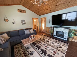 A cozy living room with a sectional sofa, a fireplace, a television, and a rug with animal prints. - Heart Lodge,slg fam sleeps 11, Lakefront great swimming / fishing kayaks, padbd. (Orland)