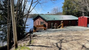 A lodge with a green roof, a red building, and a wooden deck by a lake. - Heart Lodge,slg fam sleeps 11, Lakefront great swimming / fishing kayaks, padbd. (Orland)