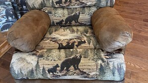 A chair with a bear-themed fabric upholstery, positioned in a room with wooden flooring and a wooden door in the background. - Heart Lodge,slg fam sleeps 11, Lakefront great swimming / fishing kayaks, padbd. (Orland)