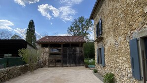Un bâtiment en pierre avec une allée gravillonnée et un espace abrité doté d’un toit en tuiles.