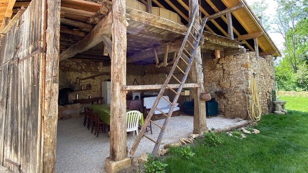 Un bâtiment rustique en bois, doté de fondations en pierre, d’un patio couvert et d’une échelle menant à un niveau supérieur.