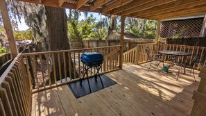 Eine Holzterrasse mit Grill, Tisch und Stühlen.