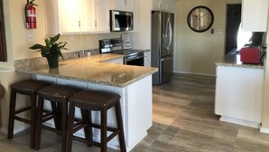 A kitchen with white cabinets, a stainless steel refrigerator, a microwave, and a clock on the wall.