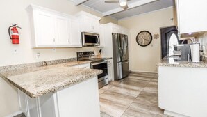 A kitchen with white cabinets, granite countertops, stainless steel appliances, and a ceiling fan.