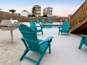 A poolside area with Adirondack chairs, a grill, and a wooden deck.