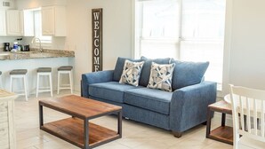 Una sala de estar moderna con un sofá azul, una mesa de centro de madera y un letrero que dice 'WELCOME'.