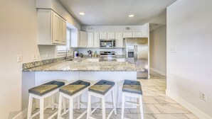Una cocina moderna con armarios blancos, encimera de granito y electrodomésticos de acero inoxidable.