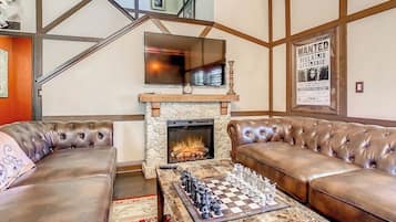 A living room with a fireplace, leather sofas, a chessboard, and a staircase.