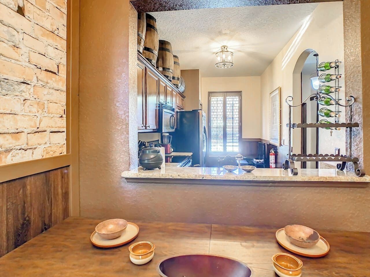 Un coin repas avec une table en bois, un mur en briques et une vue sur une cuisine avec une fenêtre.