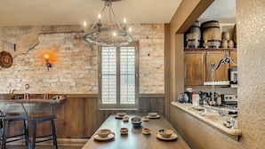 A rustic kitchen with a long wooden table set for dining, a brick wall, and wooden cabinets. - Harry Potter House at Regal Palms | Sage Vacations (Davenport)
