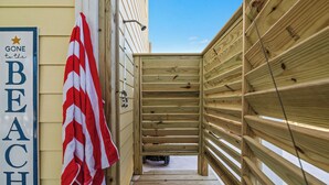 Une terrasse en bois menant à une maison de plage, sur laquelle est affiché un panneau indiquant : « JE SUIS À LA PLAGE ».